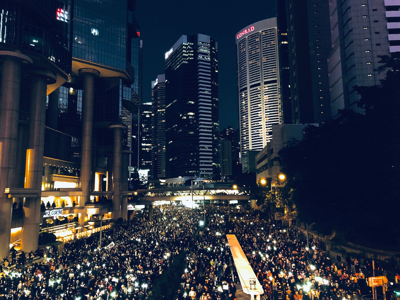 From above of crowd of people standing on street in dark modern city centre during mass protest