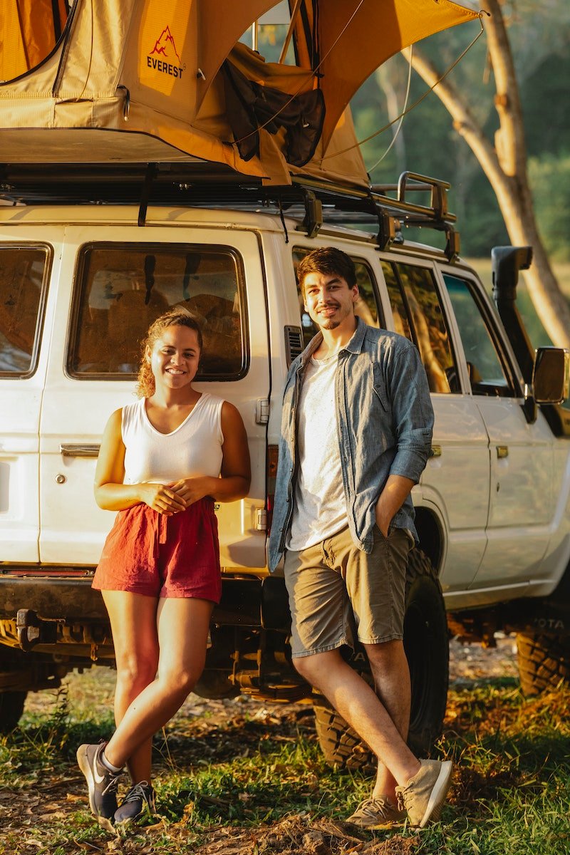 Cheerful diverse couple recreating near camping tent in green forest